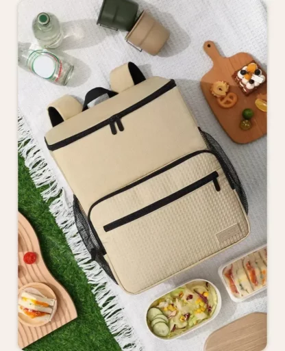 Sand-coloured cooler backpack on a picnic blanket next to food