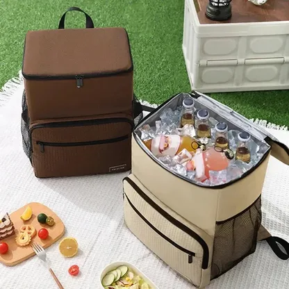 Brown and sand-coloured cooler backpacks on a picnic blanket, one open and full of drinks and ice