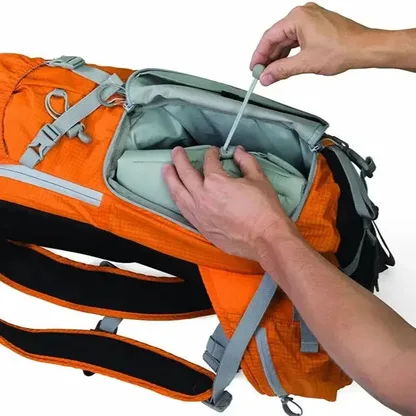 Hands opening the side access of the orange backpack to its padded camera compartment