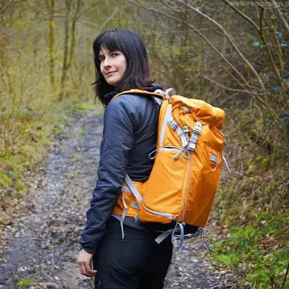 Woman on a forest path wearing the orange backpack, looking back