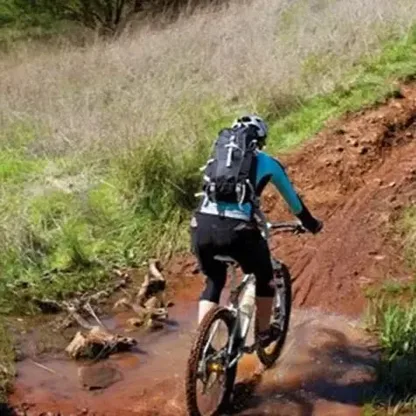 Mountain biker riding through a muddy stream wearing the black backpack